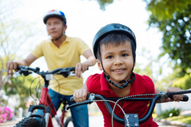 Happy mixed-race boy and his father cycling in the park